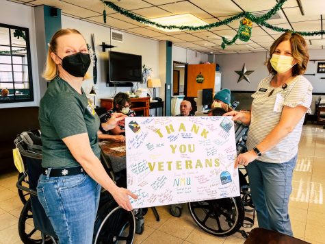 VOLUNTEERING FOR VETERANS - CSE graduate assistant Mandy Bonesteel (left) and Volunteer Coordinator for the Veterans Center Sarah Johnson (right) pose with a thank you poster signed by NMU student volunteers. Behind them senior Chloe Garr plays cards with the veterans. 